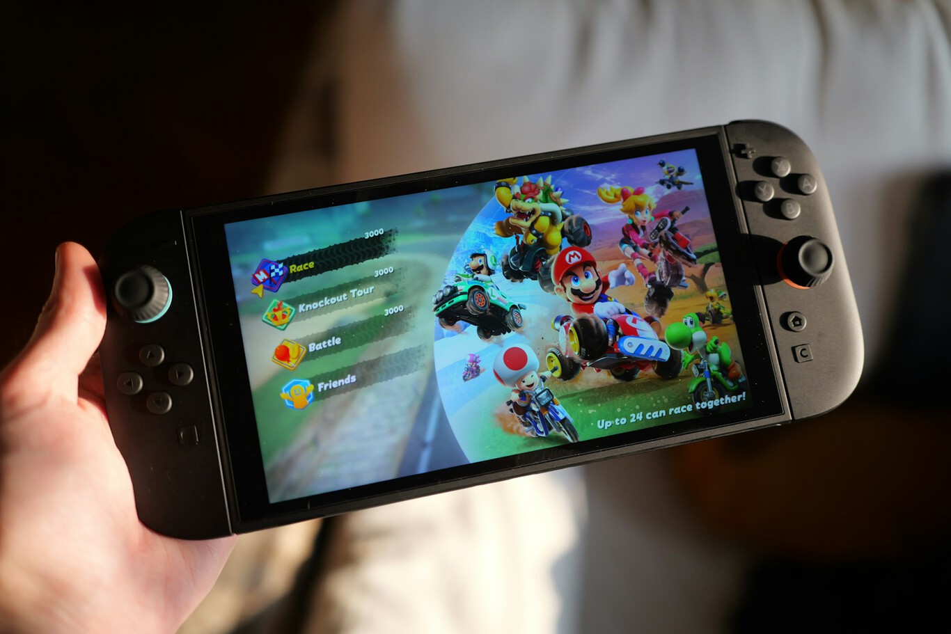 Console Nintendo Switch 2 nas mãos de uma pessoa, exibindo a tela de seleção de modos do Mario Kart World com personagens como Mario, Bowser e Yoshi