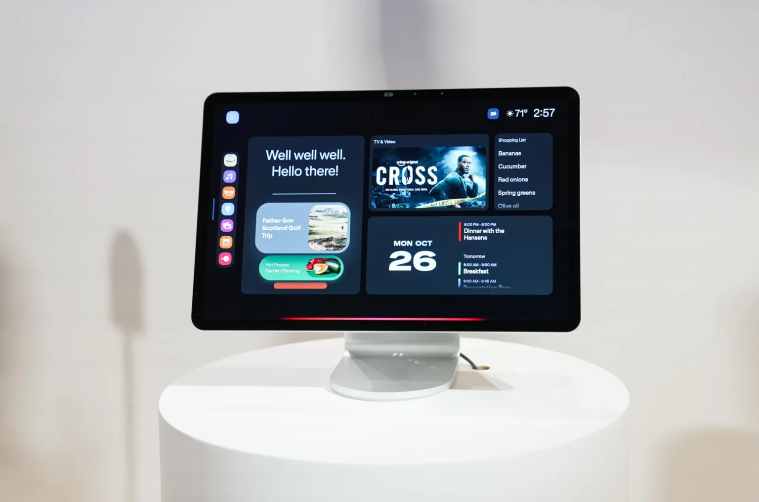 Dispositivo Amazon Echo Show 16 em base branca mostrando na tela painel doméstico com saudação, lista de compras, agenda, recomendação de filme e cartões de at…