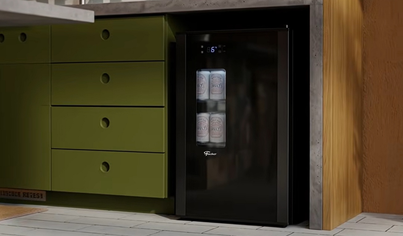 Cervejeira preta Fischer com porta de vidro, exibindo latas de cerveja na prateleira, instalada sob bancada em cozinha com armários verdes