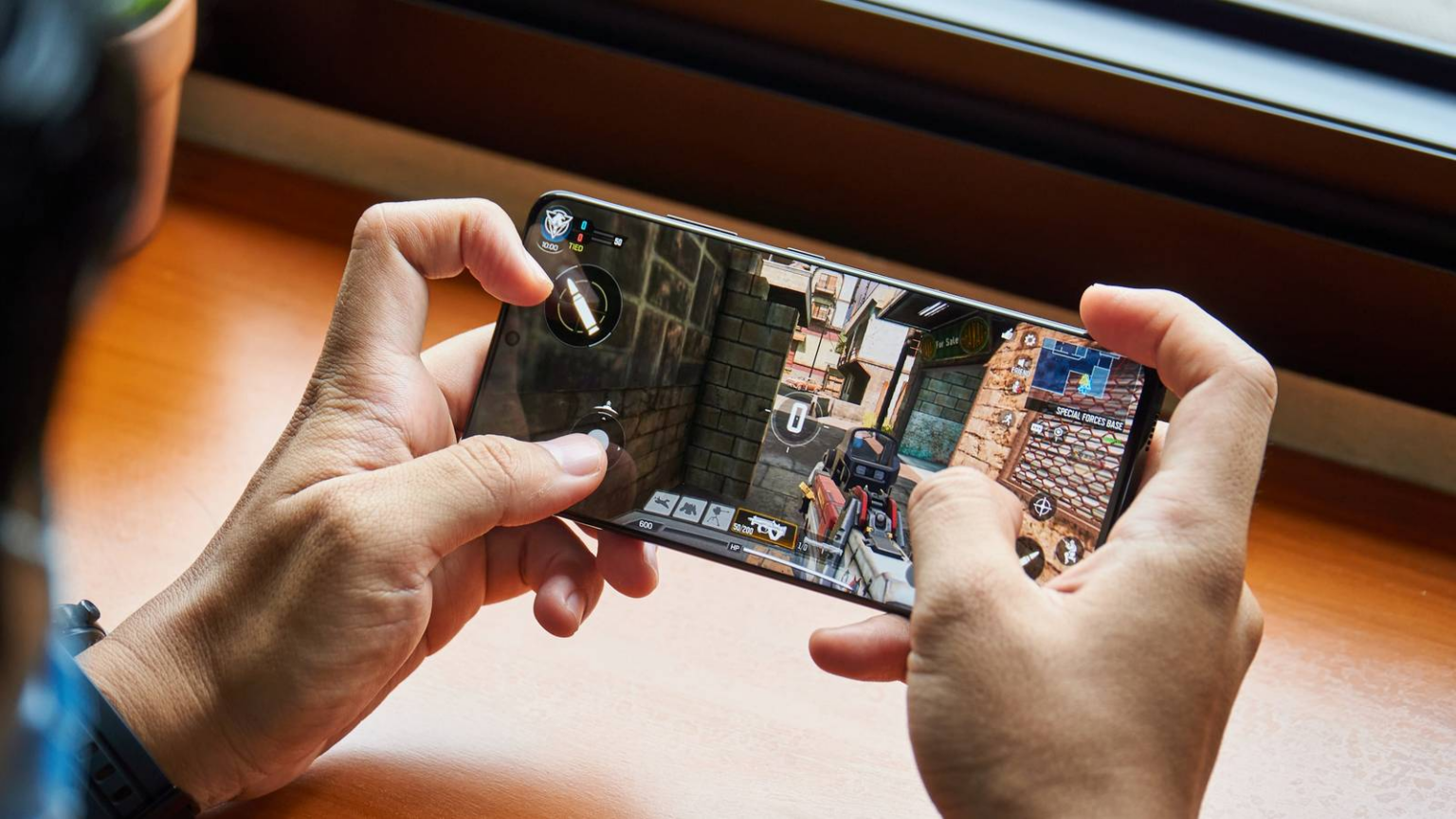 Pessoa jogando um shooter em celular Samsung Galaxy na horizontal, com controles na tela e cenário de rua urbana exibido no display