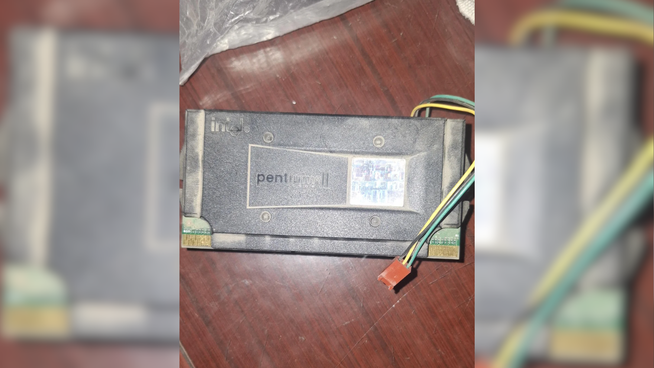 Processador Intel Pentium II em cartucho preto com etiqueta, fios coloridos e conector vermelho sobre mesa de madeira