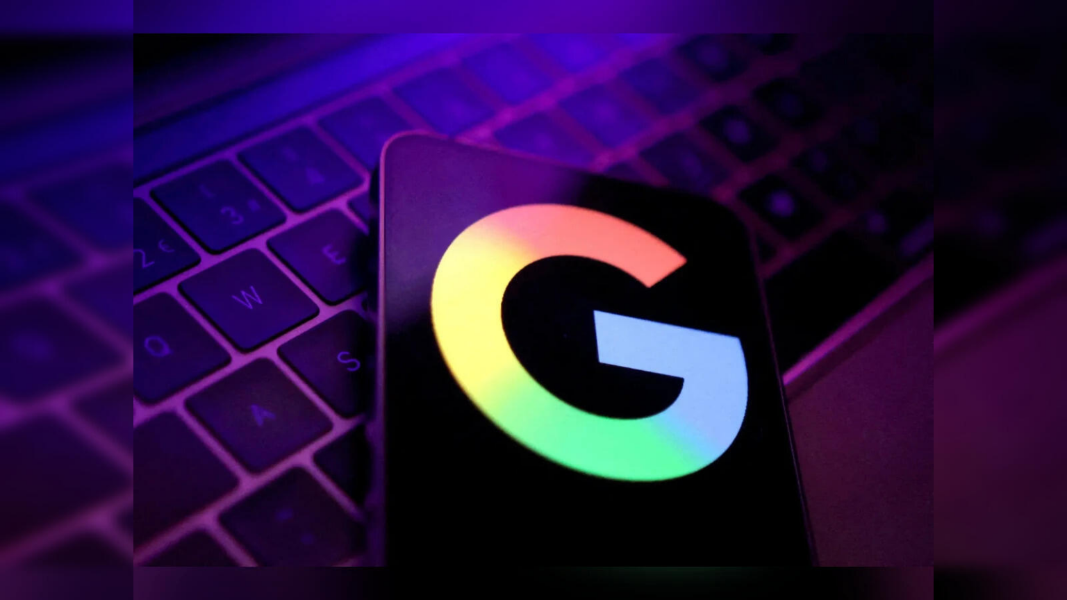 Logotipo do Google em cores em um celular escuro apoiado sobre um teclado de notebook iluminado em tons roxos