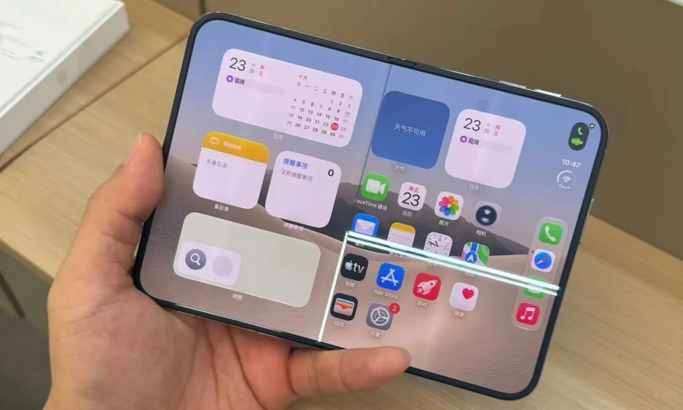 Smartphone dobrável de tela aberta na horizontal, segurado por uma mão, exibindo a tela inicial do iOS com widgets e um vinco visível no meio do display
