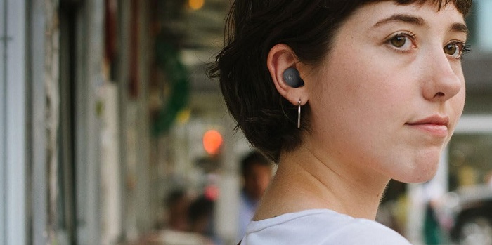 Mulher de cabelo curto olhando por cima do ombro com um fone sem fio intra-auricular preto na orelha, em rua urbana