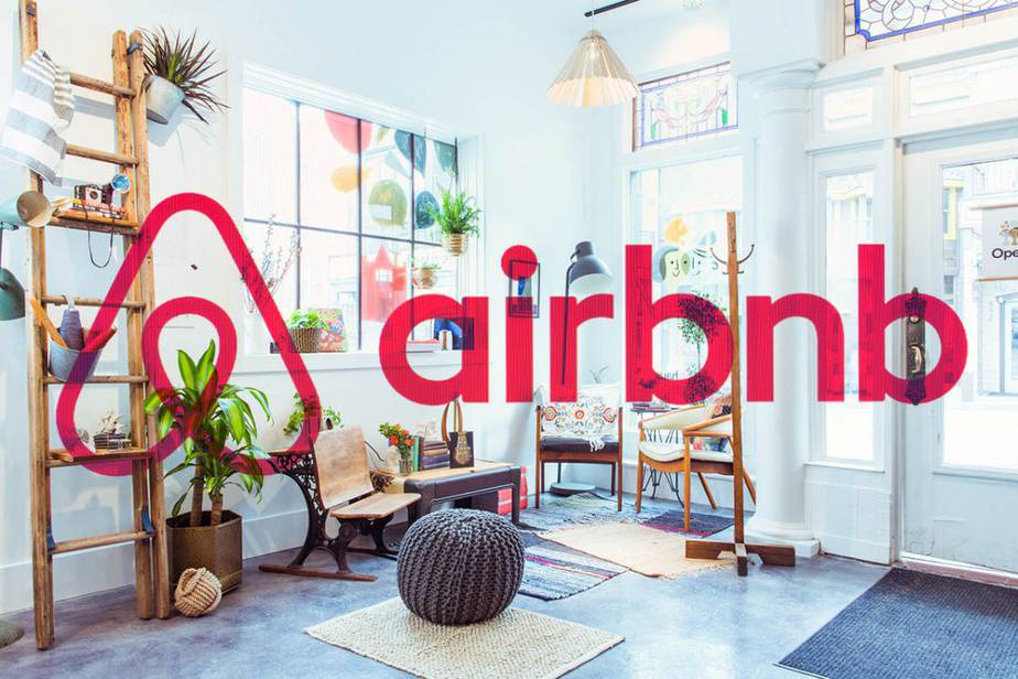 Logo vermelho do Airbnb sobreposto a um interior aconchegante com plantas, escada de madeira, poltronas e tapetes