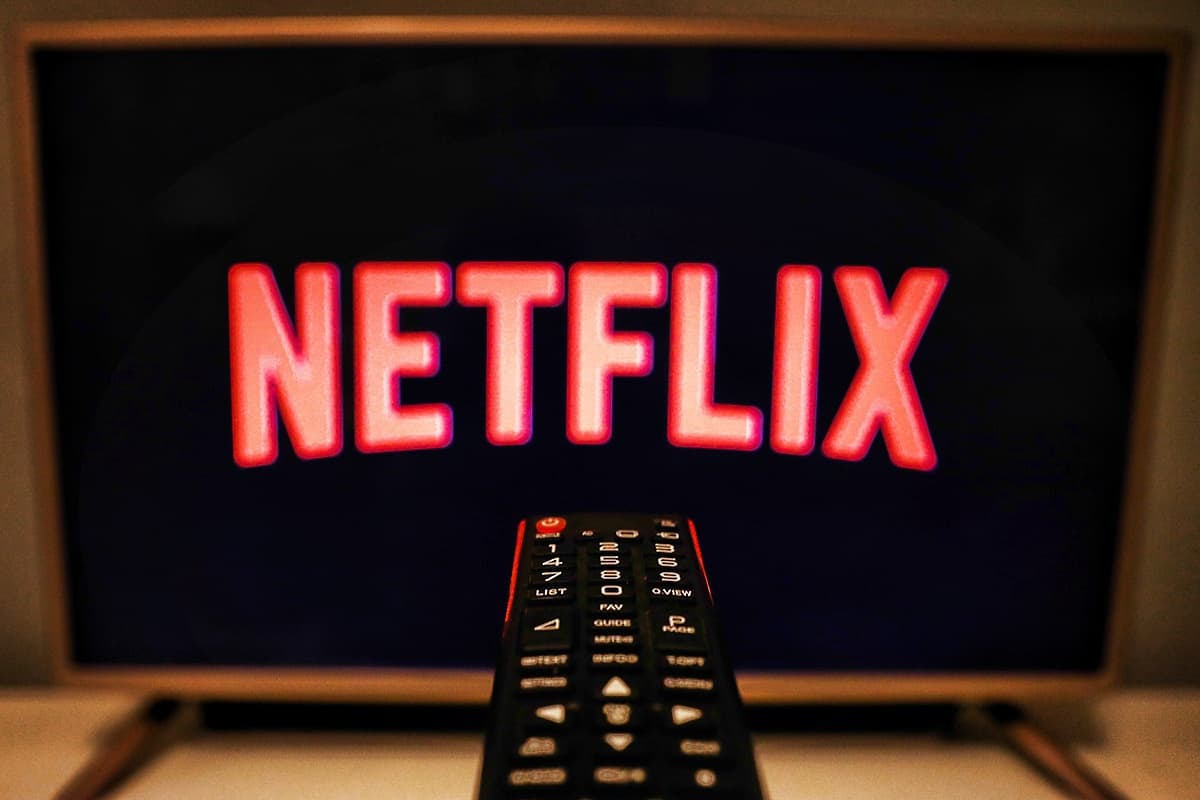 Televisão exibindo o logotipo vermelho da Netflix sobre fundo escuro, com um controle remoto preto em primeiro plano