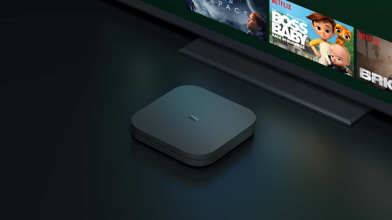Xiaomi TV Box 4S Max, pequeno receptor preto sobre uma superfície escura, ao lado de uma TV exibindo a interface da Netflix com o filme O Bebê Chefe