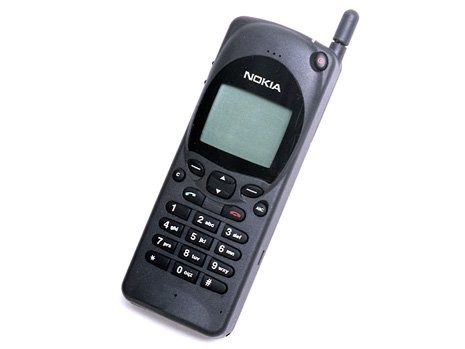 Celular Nokia 2110 preto com antena externa, tela monocromática pequena e teclado numérico com botões arredondados, sobre fundo branco
