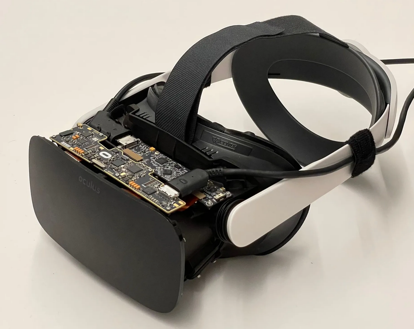 Headset de realidade virtual Oculus com a placa eletrônica exposta, com cabos conectados e tiras brancas e pretas na lateral