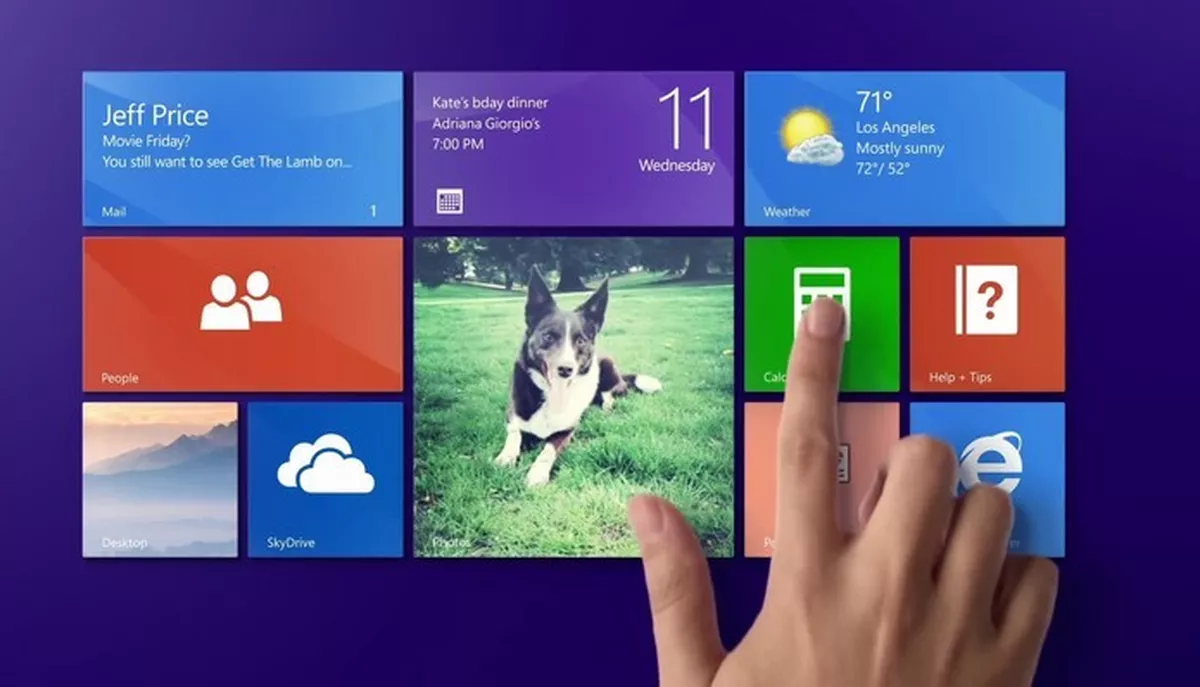 Interface do Windows 8 com blocos coloridos de aplicativos como Mail, Clima, Calendário e Internet Explorer, sendo tocada por uma mão