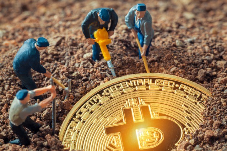 Miniaturas de mineiros escavando o solo ao redor de uma moeda dourada de bitcoin, simbolizando a mineração de criptomoedas