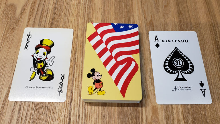 Baralho da Nintendo com carta curinga do Pinóquio, verso com Mickey Mouse diante de bandeira dos EUA e Ás de espadas Nintendo sobre mesa de madeira