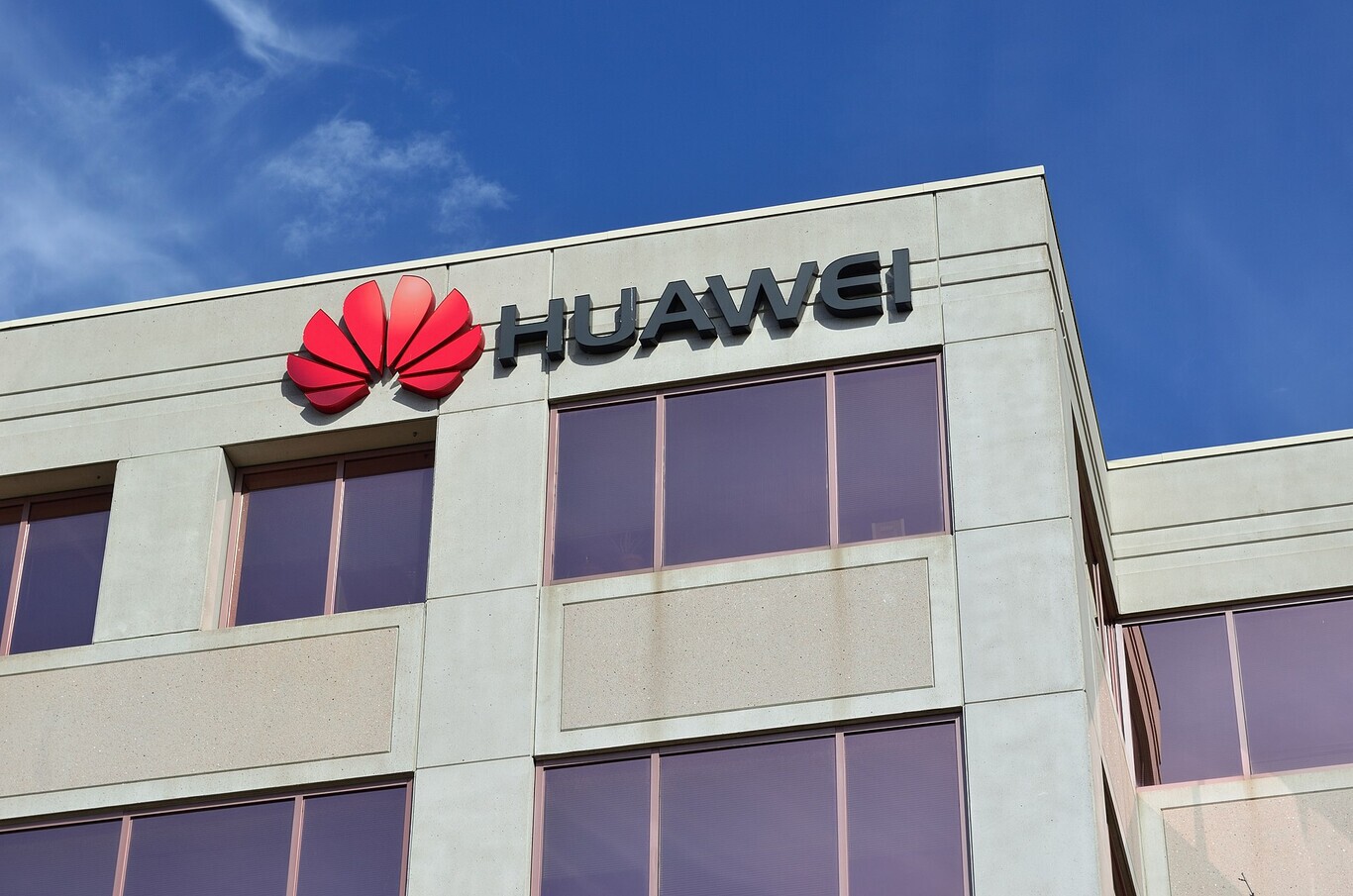 Fachada de prédio de concreto com o logotipo vermelho e o nome "HUAWEI" em letras pretas no alto, contra céu azul