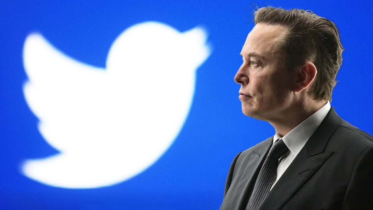 Homem de terno escuro e gravata olha para o lado, diante de um fundo azul com o logo de pássaro branco do Twitter