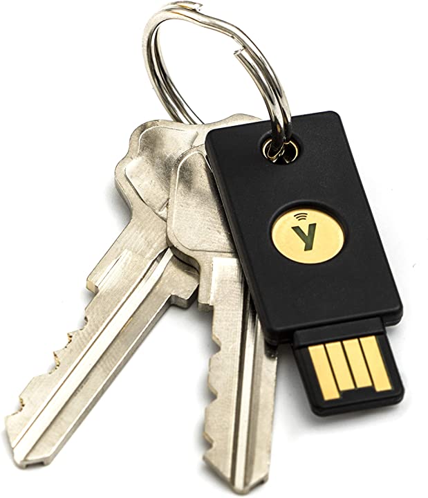 Chave de segurança YubiKey preta com conector USB dourado presa a um chaveiro junto de duas chaves metálicas comuns