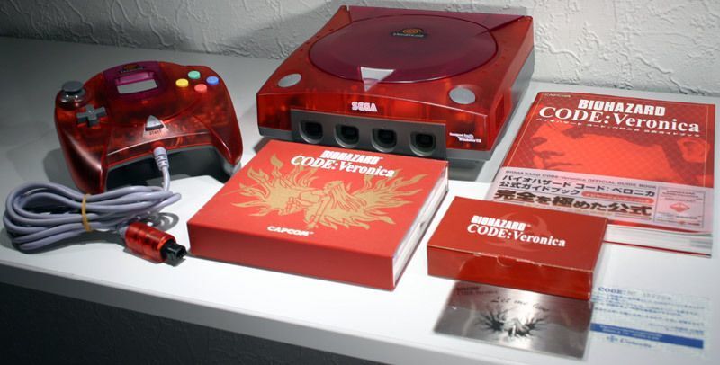 Console Sega Dreamcast em edição translúcida vermelha, com controle, jogo Resident Evil Code: Veronica e guia oficial ao lado