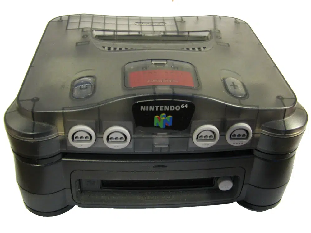 Console Nintendo 64 com carcaça translúcida cinza fumê, vista frontal, com os quatro controles e o drive de expansão 64DD na parte inferior