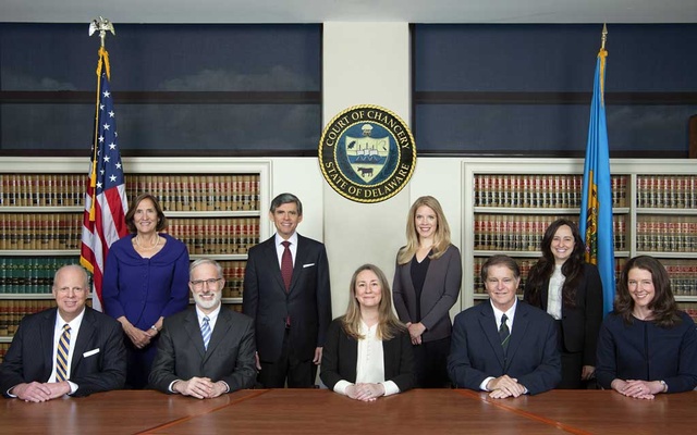 Grupo de juízes posando em sala de tribunal com estantes de livros jurídicos, bandeiras dos EUA e de Delaware e o brasão do Court of Chancery