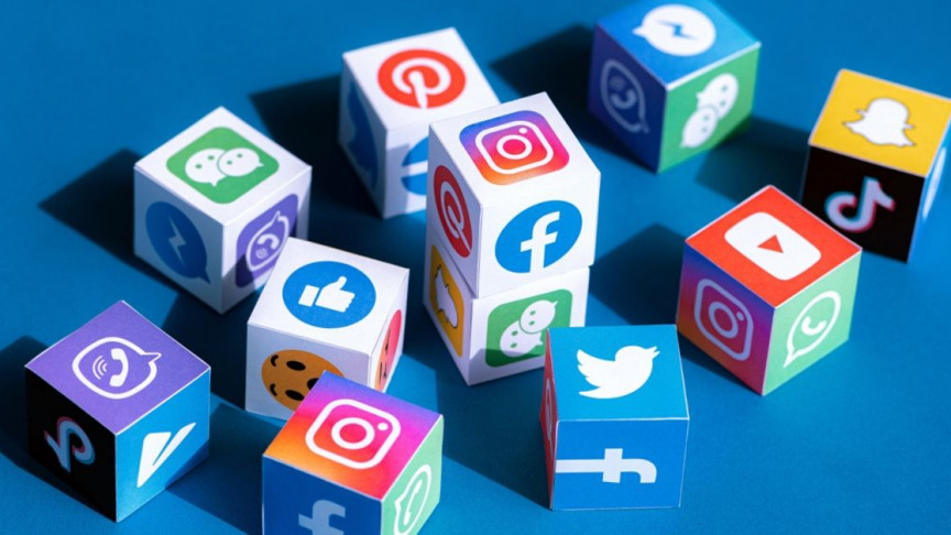 Cubos de papel com logotipos de redes sociais como Instagram, Facebook, X (Twitter), YouTube, WhatsApp, Pinterest, TikTok e Snapchat sobre fundo azul