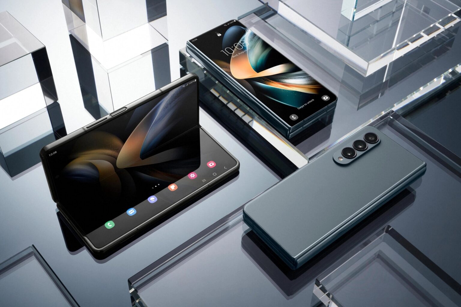 Smartphones dobráveis Samsung Galaxy Z Fold 4 em tons de cinza e verde sobre superfície de vidro, um deles aberto mostrando a tela interna