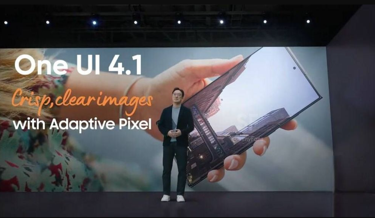 Apresentador em palco diante de telão com a frase "One UI 4.1: Crisp, clear images with Adaptive Pixel" e um smartphone gigante ao fundo