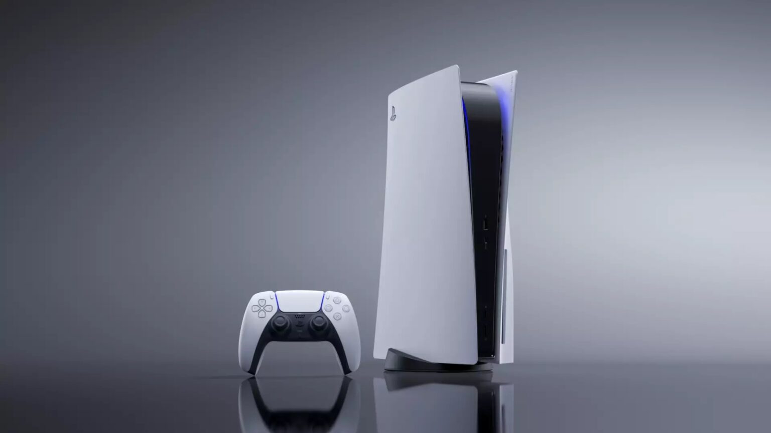 Console PlayStation 5 na posição vertical, de cor branca e preta, ao lado do controle DualSense sobre superfície cinza reflexiva