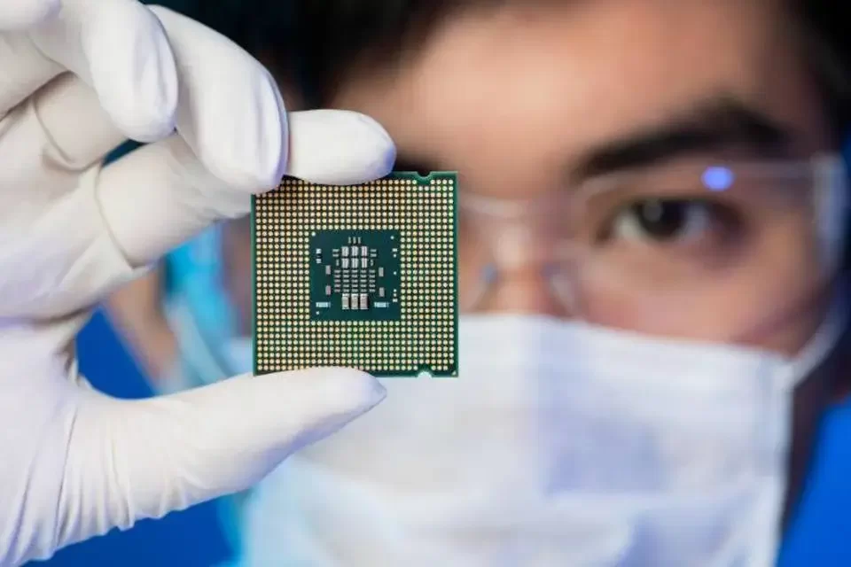 Técnico de jaleco branco e máscara segura um processador de computador com luvas brancas, com o chip em destaque em primeiro plano