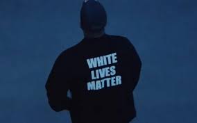 Homem de costas, de moletom preto com a frase "WHITE LIVES MATTER" estampada, em cenário azulado e escuro