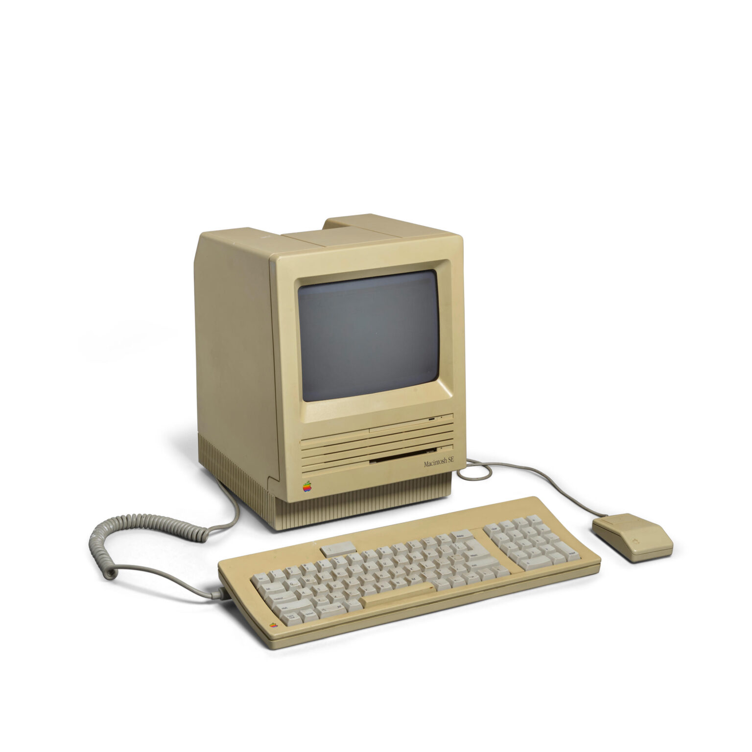 Computador Macintosh SE da Apple, de cor bege, com teclado e mouse, em fundo branco