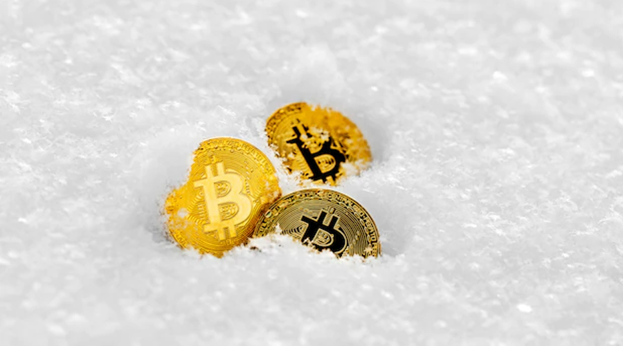 Moedas douradas de bitcoin semienterradas na neve branca, com o símbolo ₿ visível em cada uma