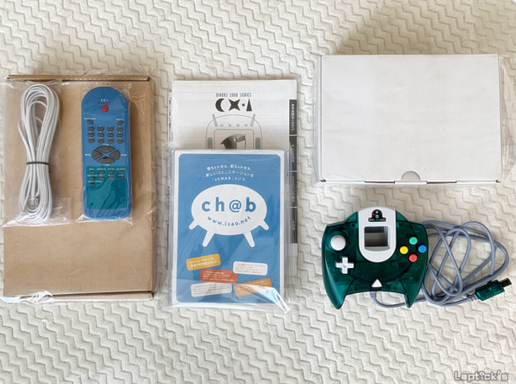 Itens da linha Dreamcast da Sega: controle verde translúcido, controle azul de TV, cabo, manual "Dreamcast" e caixa branca com livreto "ch@b