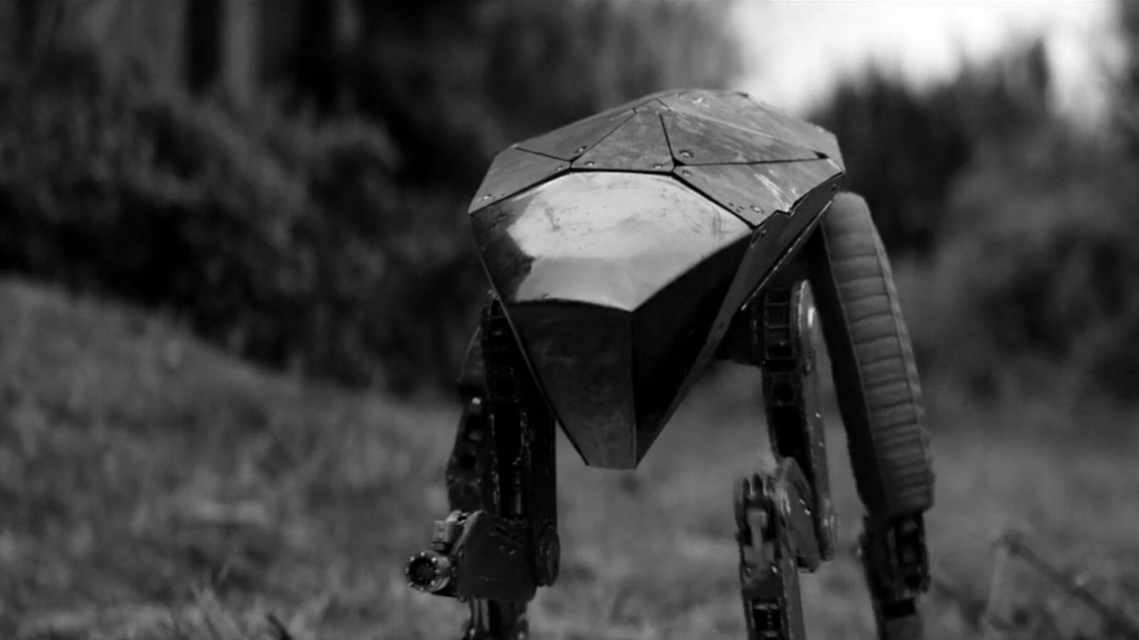 Robô de quatro patas com carcaça metálica facetada e pernas articuladas, em preto e branco, caminhando sobre um gramado (cena do episódio Metalhead de Black Mi…