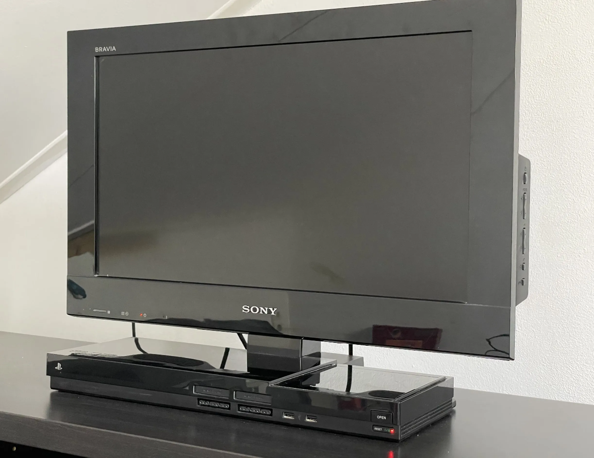 TV Sony Bravia de tela escura sobre console PlayStation 2 de design preto, apoiada em um móvel de madeira escura