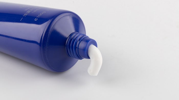 Tubo azul de pasta de dente com a pasta branca saindo pelo bico, sobre fundo branco
