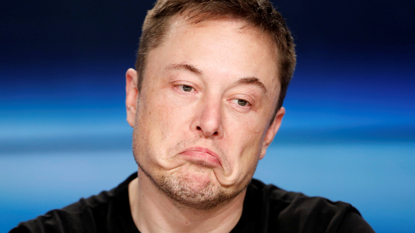 Homem de cabelo curto e barba por fazer, com camiseta preta, fazendo expressão de desânimo com os lábios projetados para baixo, em fundo azul desfocado