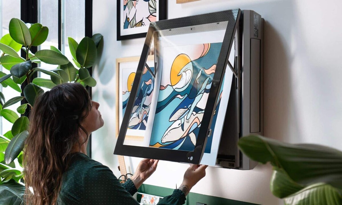 Mulher de cabelo castanho ajusta um painel de tela de 27 polegadas instalado na parede de uma sala decorada com plantas e quadros ilustrados