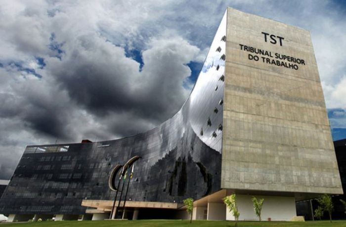 Edifício do Tribunal Superior do Trabalho (TST) em Brasília, com fachada curva espelhada sob céu nublado e o letreiro "TST - Tribunal Superior do Trabalho
