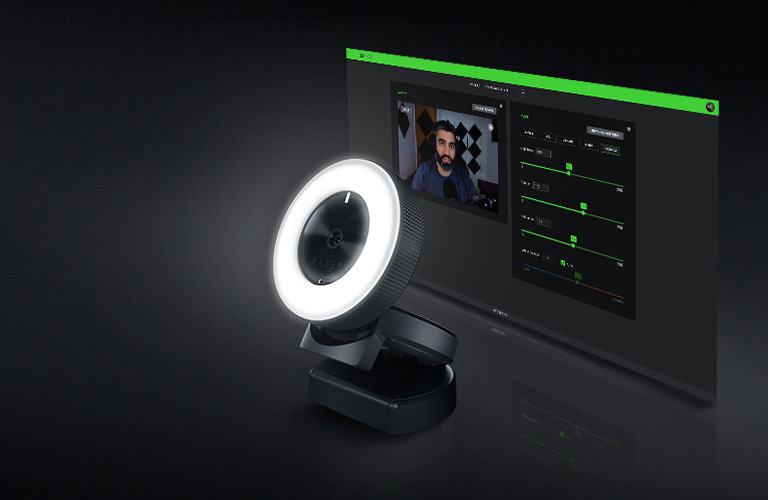 Webcam Razer Kiyo com anel de luz ativo ao lado de monitor exibindo o software Razer Synapse com ajustes de imagem