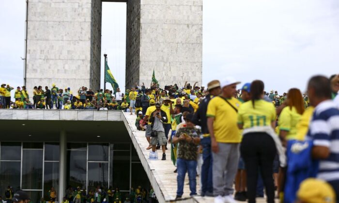 Multidão vestida de verde e amarelo sobe a rampa e ocupa a cobertura de um prédio com colunas de mármore em Brasília, ao lado de bandeiras