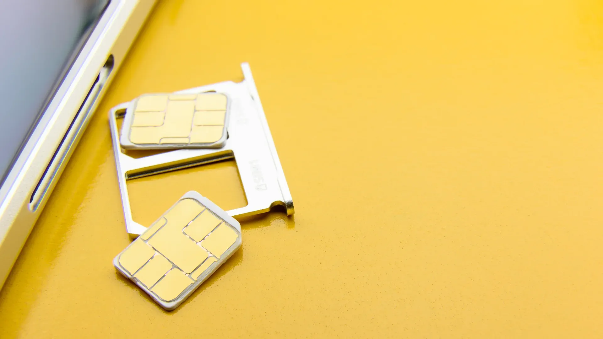 Bandeja de chip SIM ao lado de um celular, com dois chips SIM dourados sobre fundo amarelo