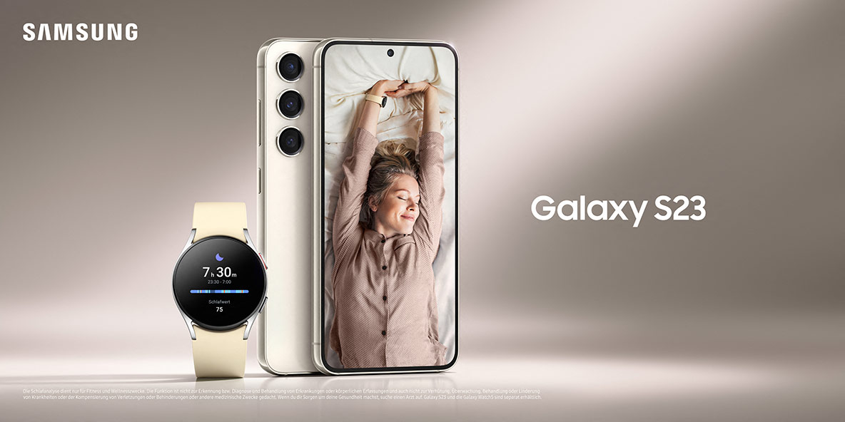 Smartphone Samsung Galaxy S23 de cor creme ao lado de um smartwatch com pulseira clara, exibindo uma mulher se espreguiçando na tela, em ambiente claro
