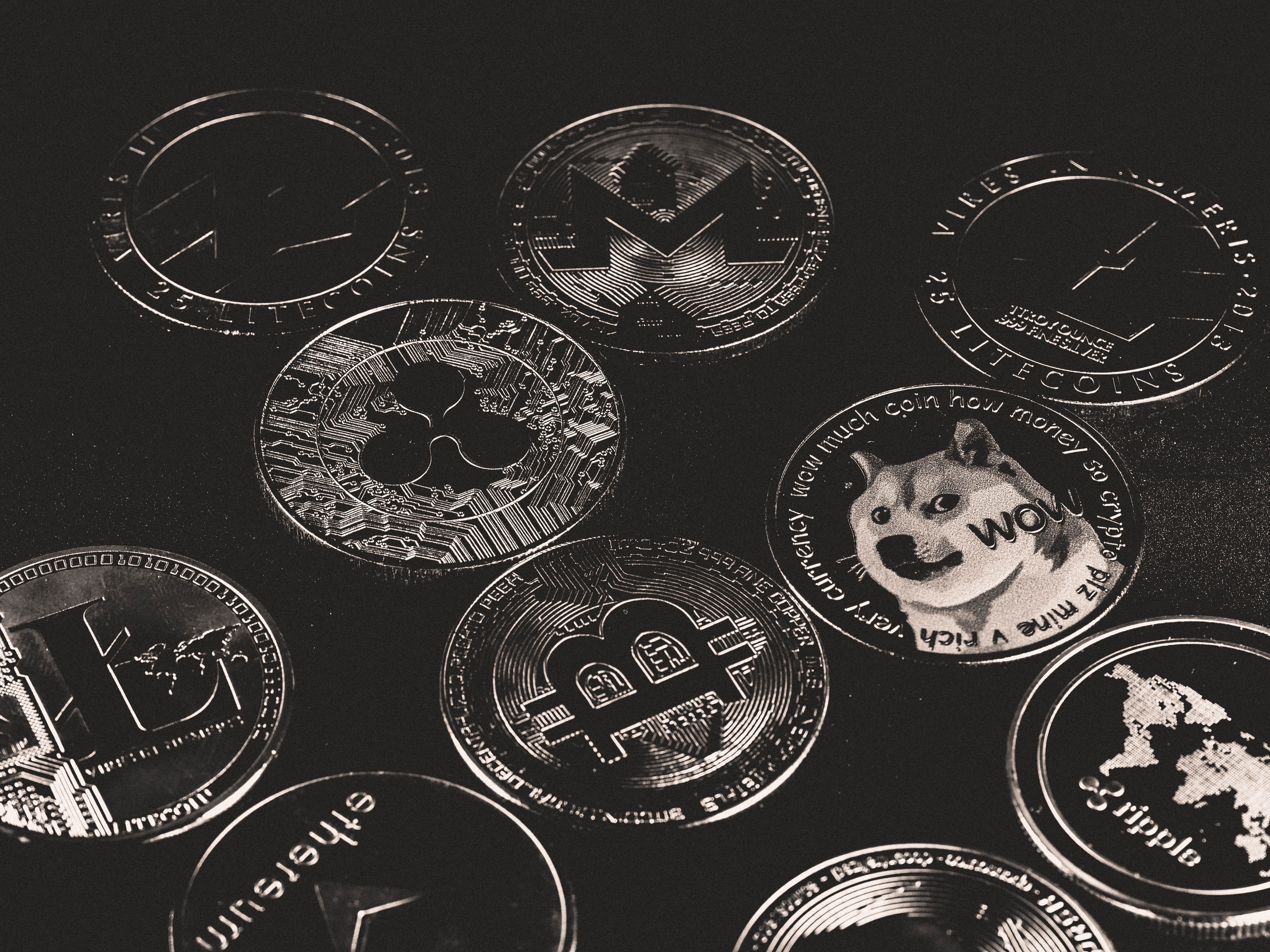 Moedas metálicas prateadas de criptomoedas, como Bitcoin, Litecoin, Ripple e Dogecoin, espalhadas sobre uma superfície escura