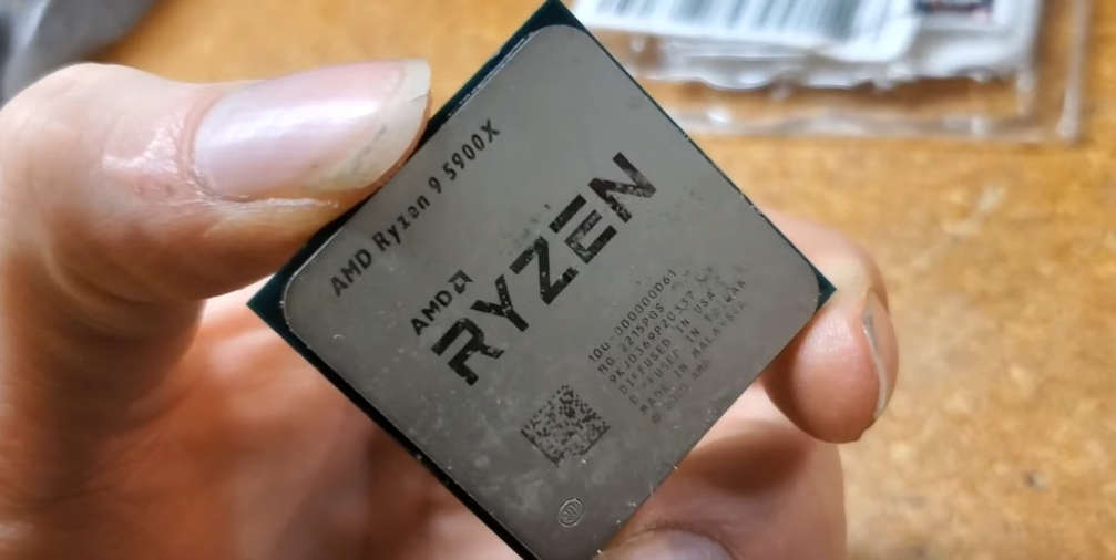 Processador AMD Ryzen 9 5900X segurado entre os dedos de uma mão, com a marcação do modelo visível sobre a tampa metálica