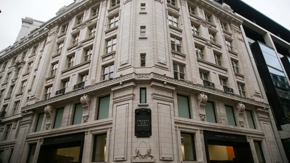 Fachada de prédio clássico de pedra clara com janelas e sacadas de ferro, com placa "Twenty Air Street" na entrada, ao lado de um edifício moderno de vidro