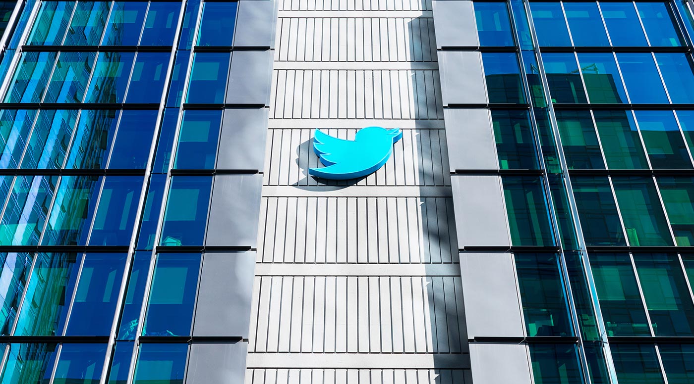 Fachada de prédio espelhado de vidro azulado com grande logotipo azul do pássaro do Twitter em destaque no centro
