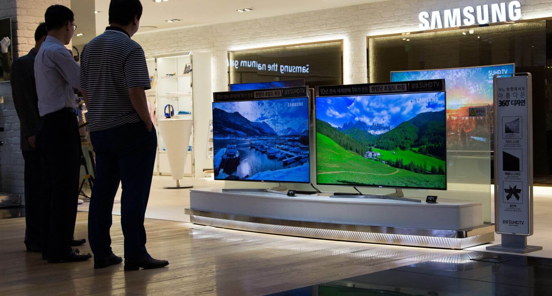 Duas TVs Samsung com paisagens na tela expostas em loja, com dois homens observando ao lado