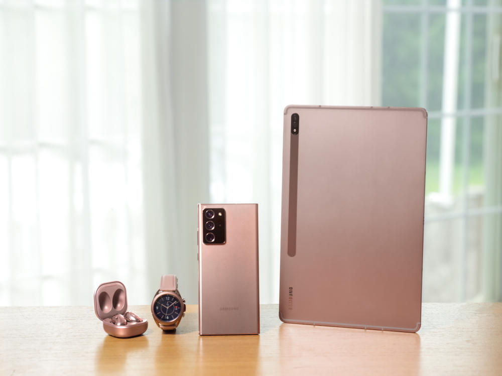 Fones Galaxy Buds Live, smartwatch Galaxy Watch, smartphone Galaxy Note20 e tablet Galaxy Tab S7 em tons de bronze sobre mesa de madeira