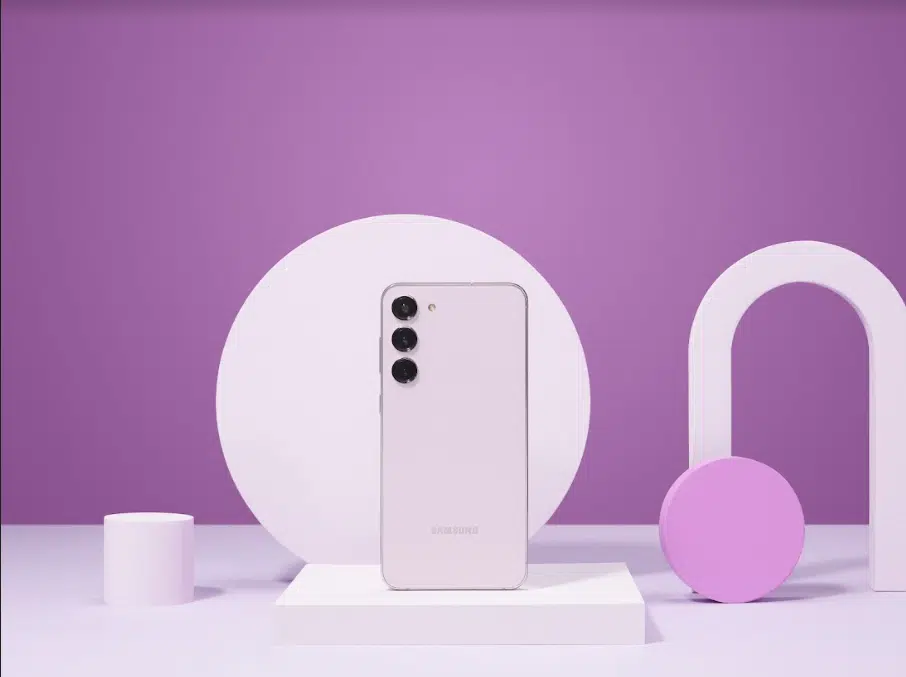 Smartphone Samsung Galaxy S23 cor creme na traseira, com três câmeras, em um cenário lilás com formas geométricas brancas