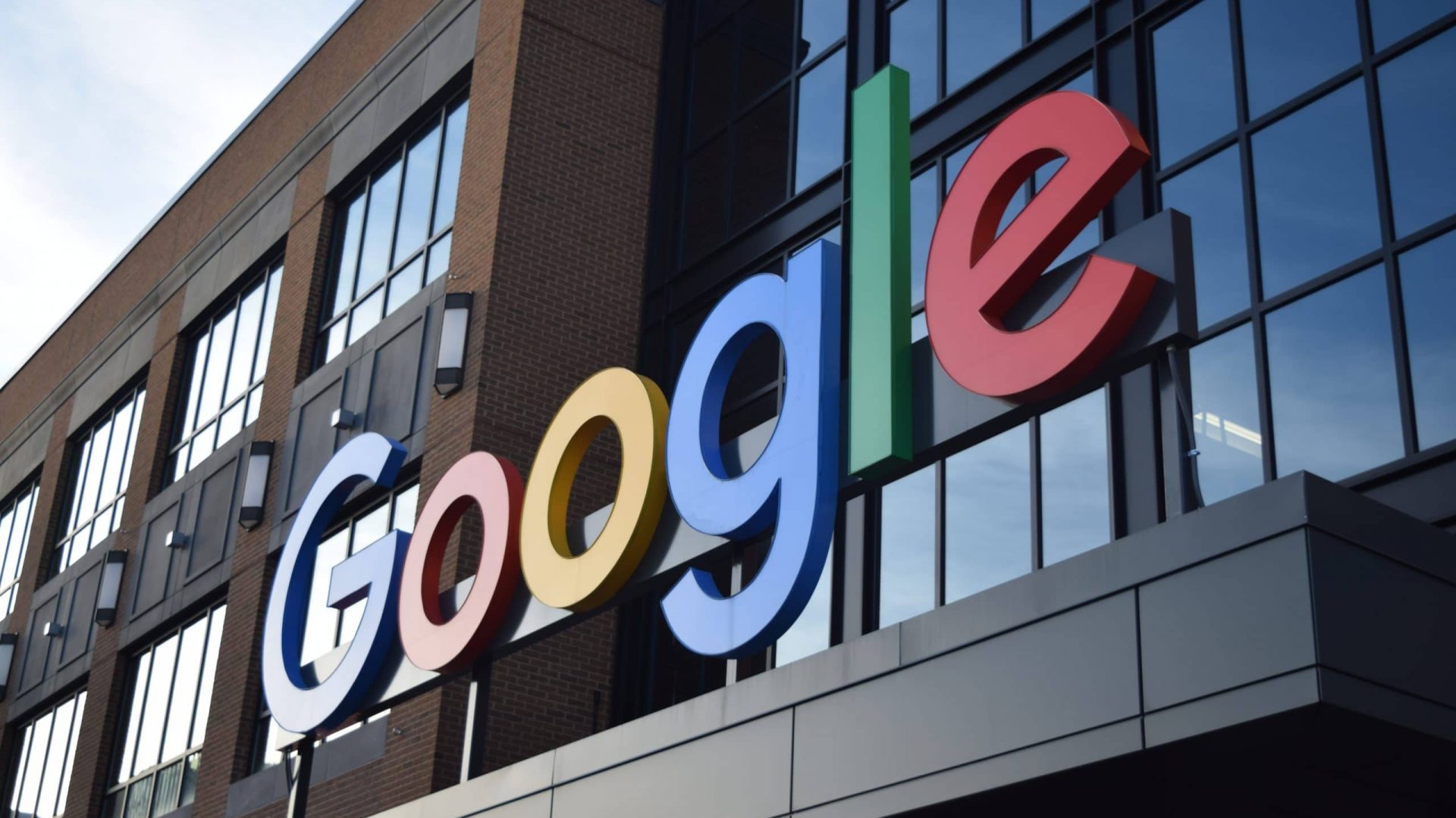 Fachada de prédio de tijolos e vidros com o logotipo colorido do Google em letras grandes e tridimensionais