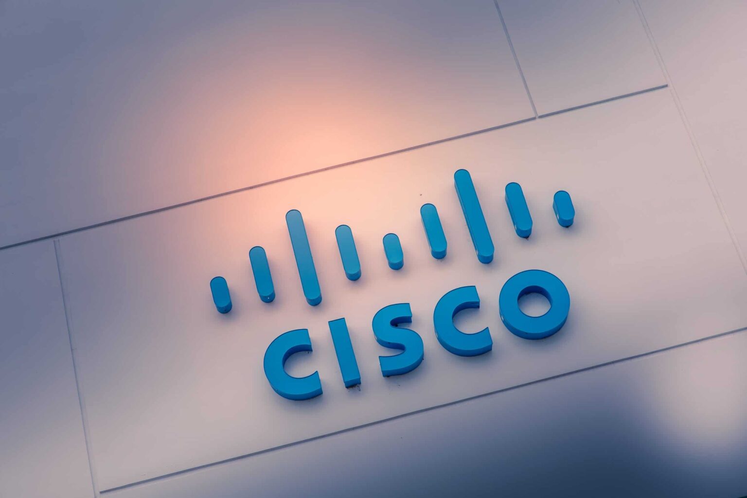 Logotipo azul em relevo da Cisco, com a marca de barras e o nome em letras maiúsculas, fixado em painel branco iluminado
